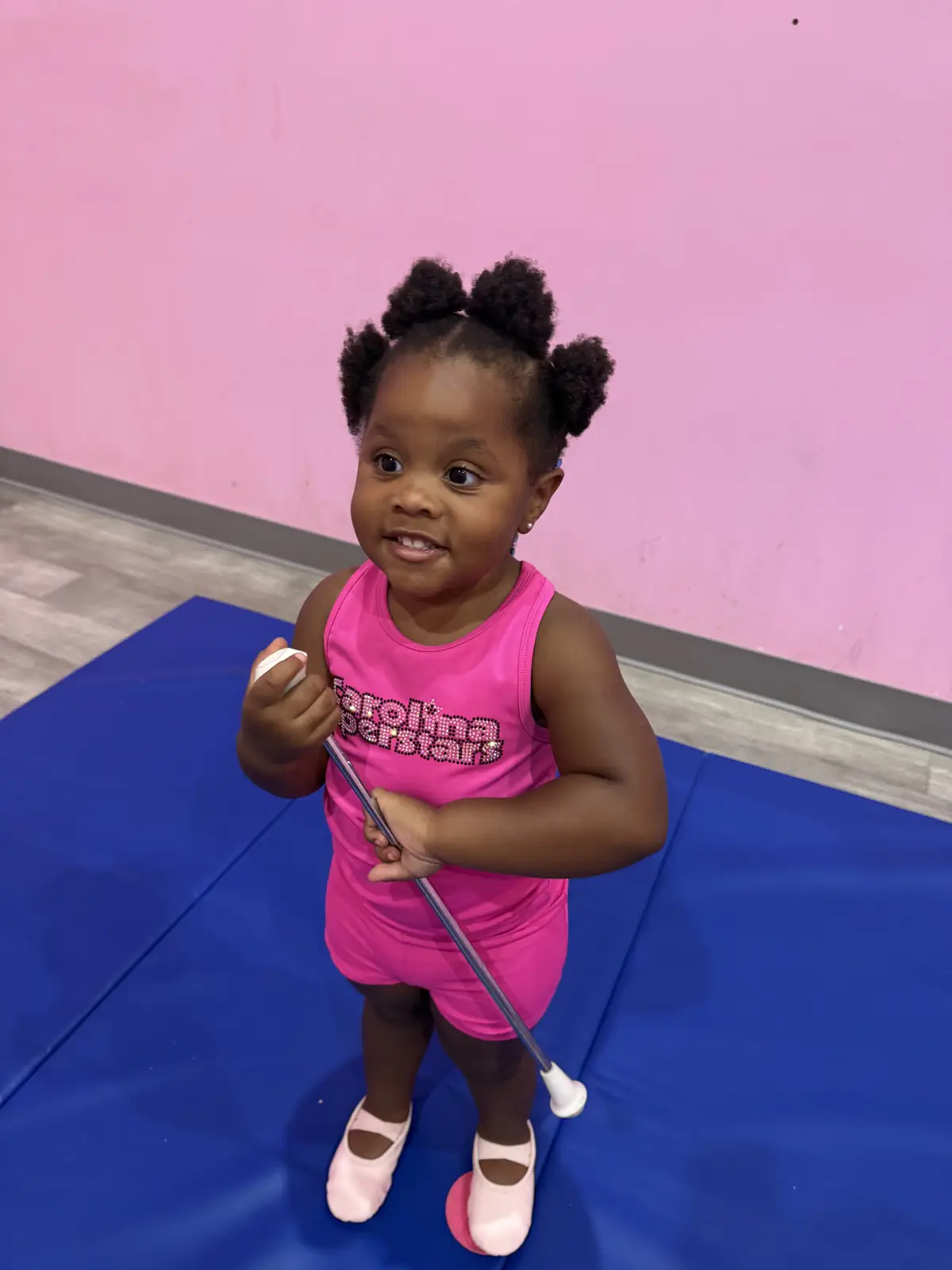 Toddler girl in pink gymnastics outfit holding a baton