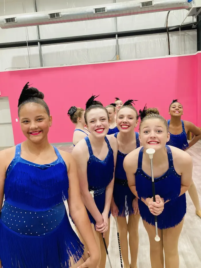 Young baton twirlers in blue fringed costumes smiling indoors