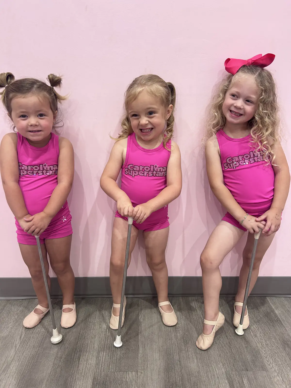 Three young girls in pink Carolina Superstars dance uniforms holding batons