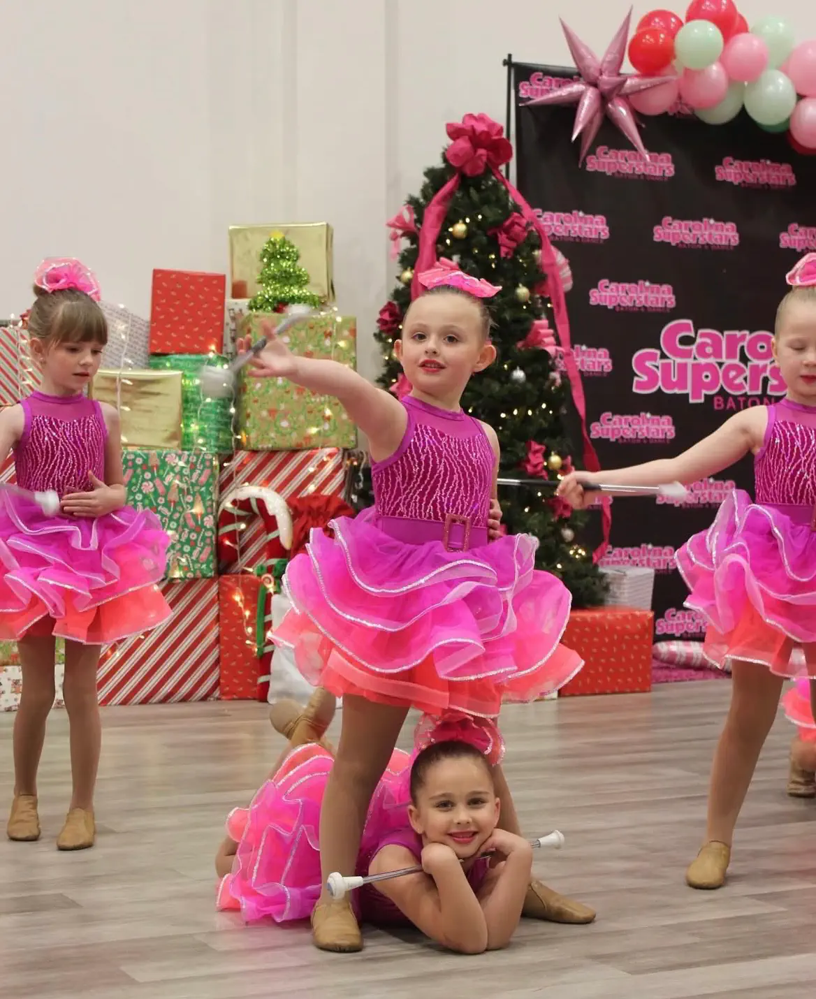 Young girls in pink costumes performing baton twirling at Christmas recital