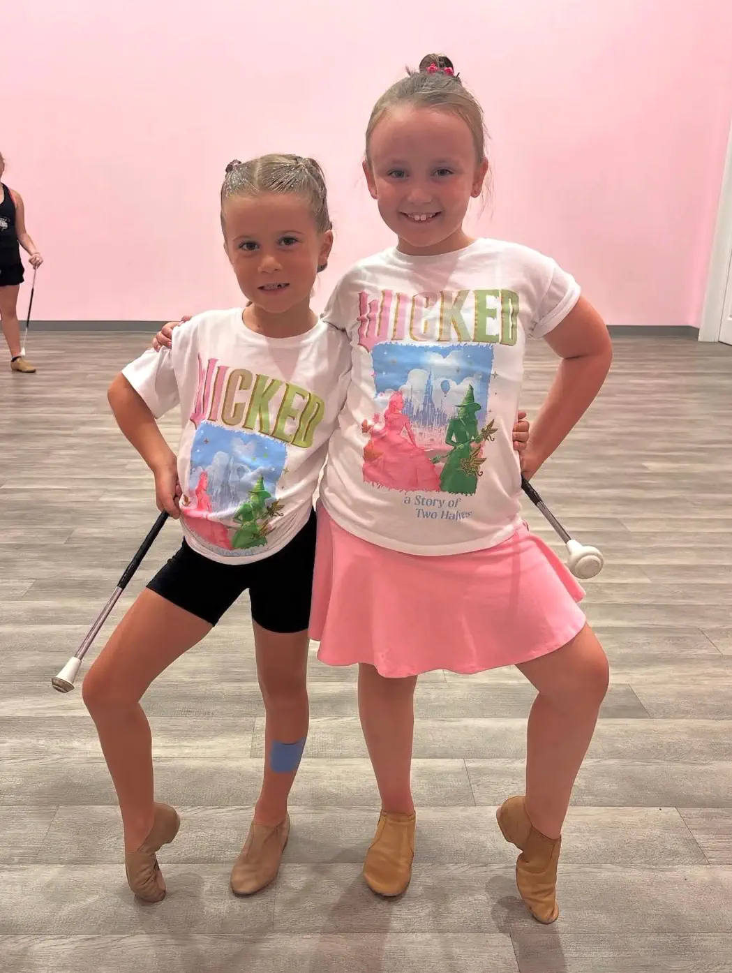 Two young girls in Wicked shirts holding batons at dance studio