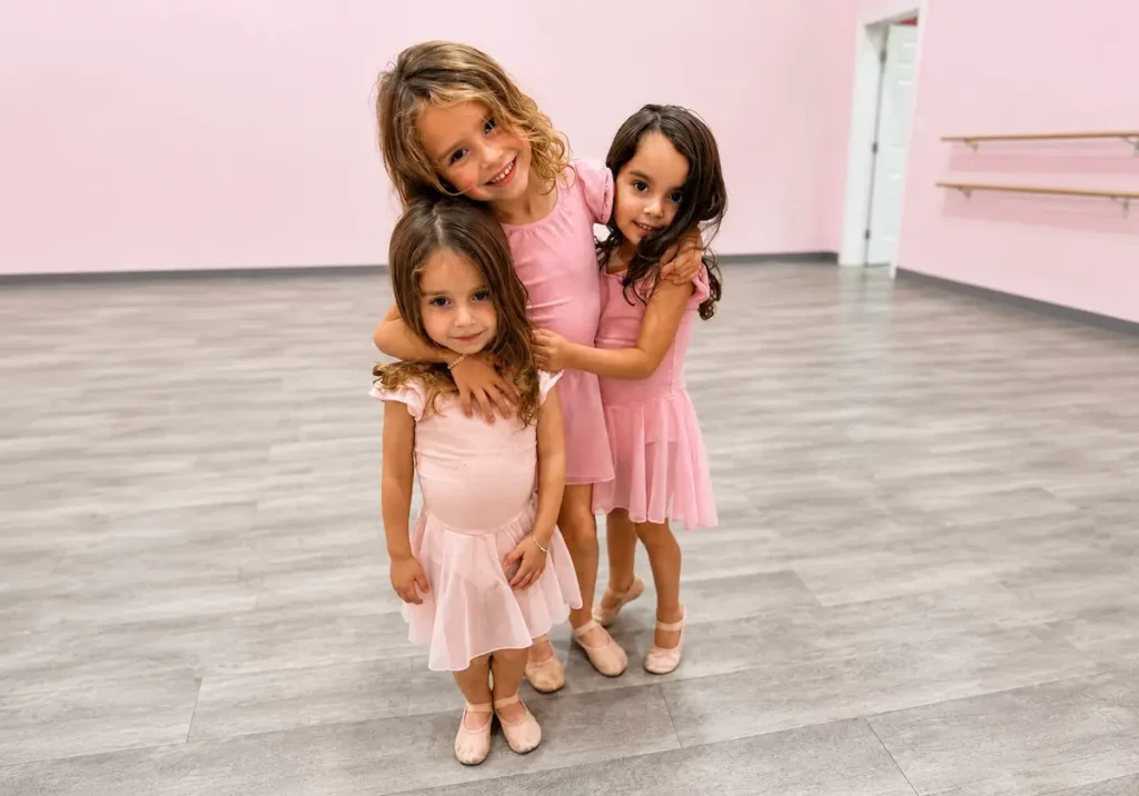 Three young girls in pink ballet outfits posing in dance studio